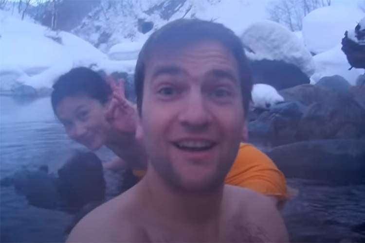 海外の方と日本人の男女のグループが雪の降る中混浴露天風呂を楽しむ様子【切明温泉】